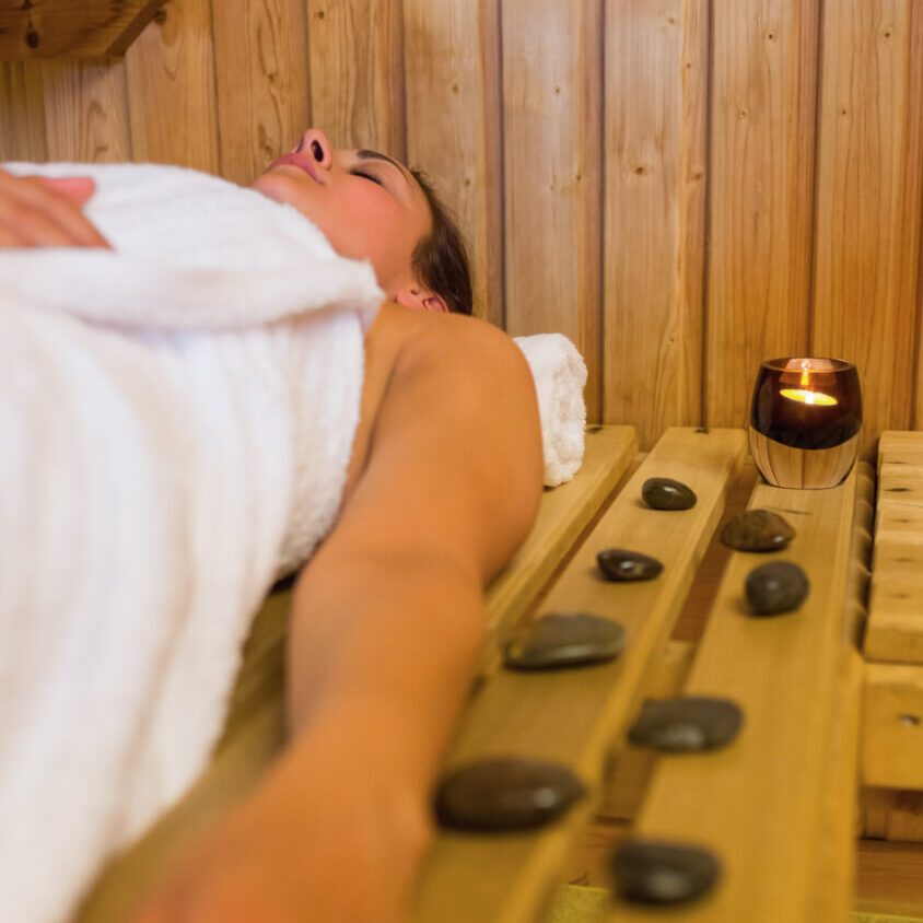 Femme qui se détend dans un sauna avec des pierres chaudes et une bougie